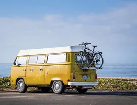 A yellow campervan driving on road near beach - listing