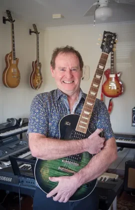 Angus Campbell holding his guitar surrounded by other instruments