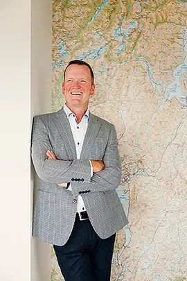 Jason McCracken new CEO MAS posing against a wall with a map on it.webp