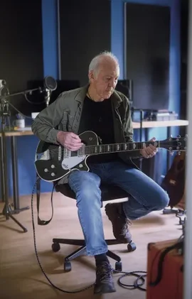 Mac Mckay playing the guitar sitting on a chair