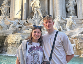 Two Travellers Diana and Josh, smiling in front of a European fountain listing