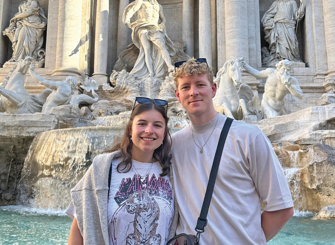 Two Travellers Diana and Josh, smiling in front of a European fountain listing